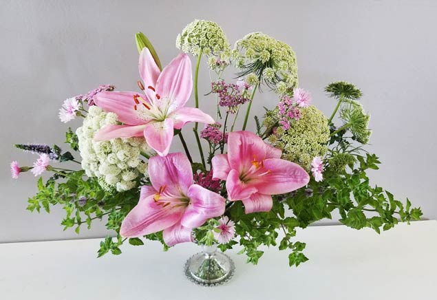 pink stargazer lilies and other flowers arranged in an urn