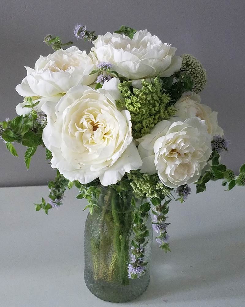 elegant white roses and other flowers arranged with mint in a small vase